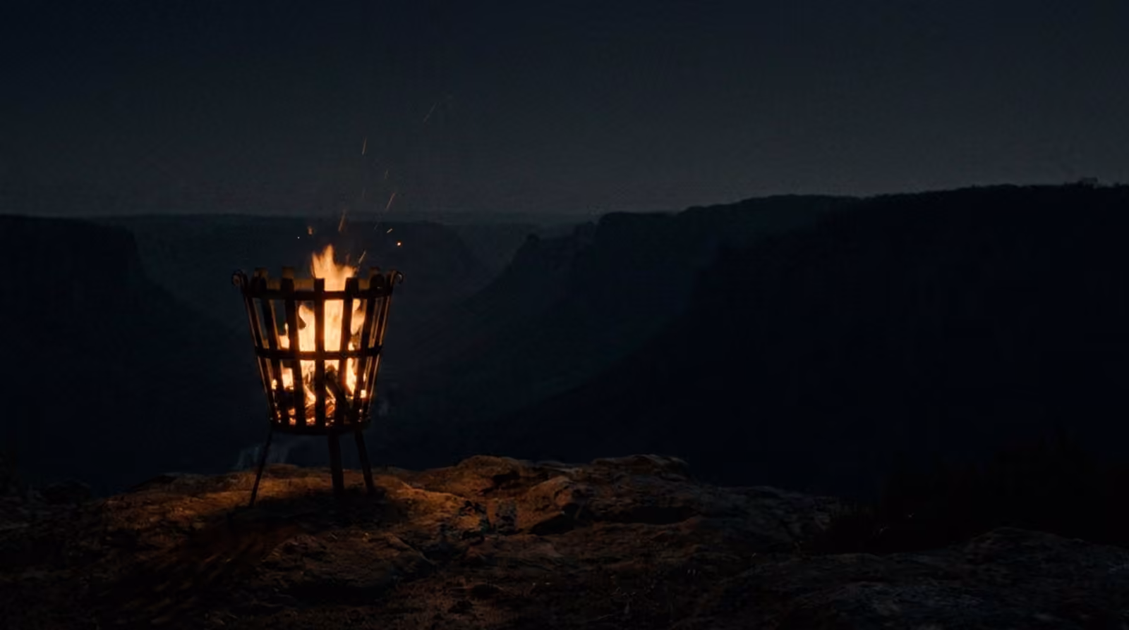 The beacon alight: one warm amber flame in the darkness, light pooling on the rock.